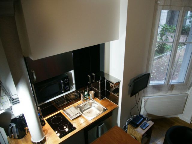 Une cuisine toute équipée associant une teinte noire et boisée - Loge de gardiens en studio moderne