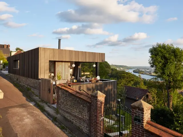 Une maison posée sur un mur en brique - Une maison en zinc noir posée sur un mur en brique