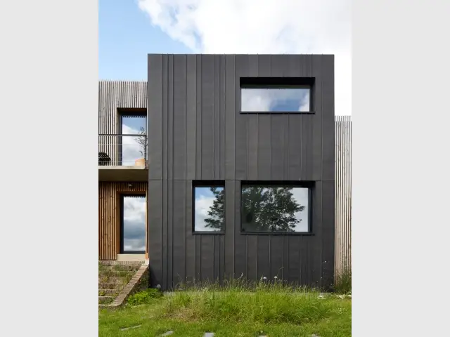 Une enveloppe en zinc noir - Une maison en zinc noir posée sur un mur en brique