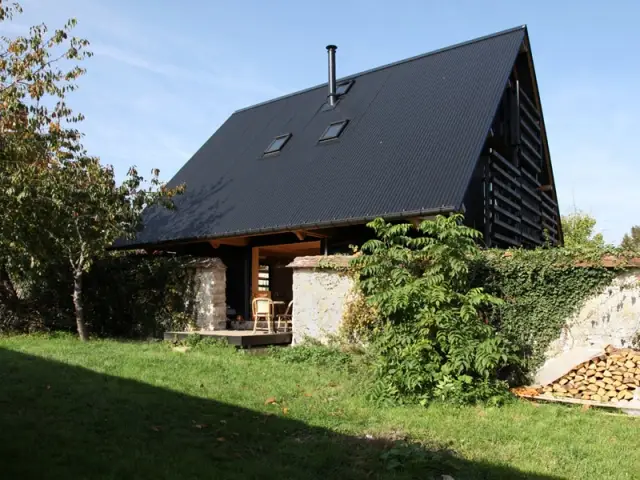 Une maison tout en bois blottie entre deux murs en pierres